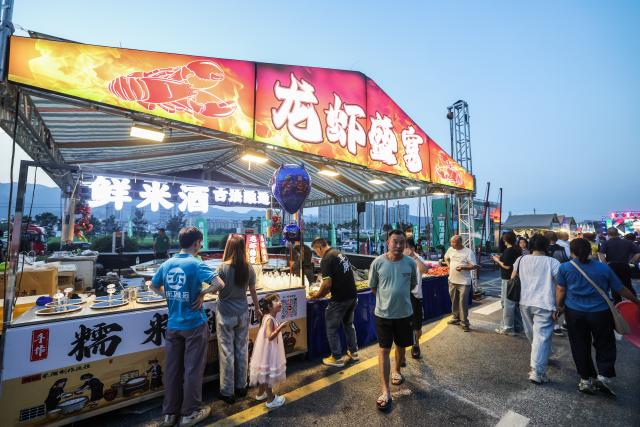 (260725) -- JIANDE, July 25, 2026 (Xinhua) -- People are seen at a beer festival in Jiande City of east China's Zhejiang Province on July 24, 2026. A summer beer festival kicked off at a farmers market here on Friday. Featuring live performances, gourmet foods and drinks, leisure activities and bazaars, the event attracted thousands of locals and tourists. (Xinhua/Xu Yu)