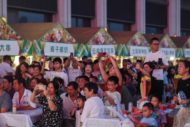 (260725) -- JIANDE, July 25, 2026 (Xinhua) -- People watch a performance at a beer festival in Jiande City of east China's Zhejiang Province on July 24, 2026. A summer beer festival kicked off at a farmers market here on Friday. Featuring live performances, gourmet foods and drinks, leisure activities and bazaars, the event attracted thousands of locals and tourists. (Xinhua/Xu Yu)