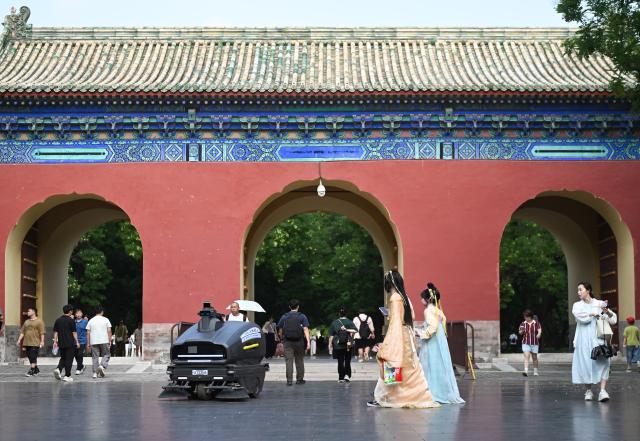 (260725) -- BEIJING, July 25, 2026 (Xinhua) -- Tourists dressed in traditional Chinese attire encounter with a cleaning robot at the Temple of Heaven Park in Beijing, capital of China, July 24, 2026. Marking the second anniversary of the successful inscription of the Beijing Central Axis on the UNESCO World Heritage List, heritage sites along the Beijing Central Axis, such as the Palace Museum, Zhengyangmen Gate, and Altar of the God of Agriculture, also referred to as the Xiannongtan Temple, will either open to the public free of charge or launch new exhibitions on July 27.
  Over the past two years, efforts to conserve, inherit and make good use of the Beijing Central Axis have advanced steadily, achieving new outcomes in areas including related legal system, UNESCO World Heritage signage, landscape improvement, creative utilization, collaborative protection and international communication. (Xinhua/Chen Zhonghao)