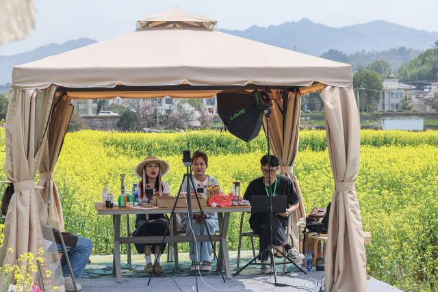 (260725) -- HANGZHOU, July 25, 2026 (Xinhua) -- People promote local cultural tourism projects beside a cole flower field in Jiande City, east China's Zhejiang Province, March 23, 2025. TO GO WITH "China Focus: Beyond livestream: Can clicks become lasting careers for China's youth?" (Xinhua/Xu Yu)