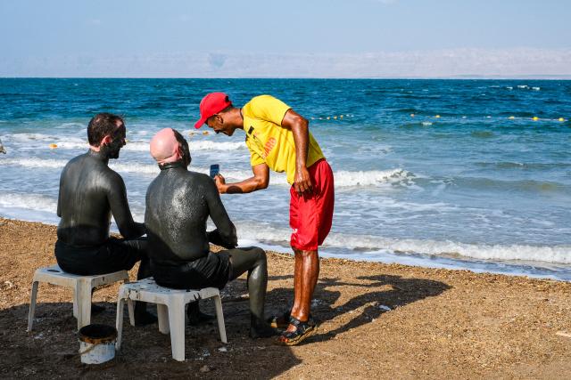 (260726) -- AMMAN, July 26, 2026 (Xinhua) -- Tourists apply Dead Sea mud to their bodies near the Dead Sea in Jordan, on July 25, 2026. The Dead Sea has been experiencing a long-term decline in its water level due to reduced inflow from the Jordan River, the region's naturally high evaporation rates, and industrial mineral extraction. Available data show that as of July 2026, the Dead Sea's surface was approximately 440 meters below sea level, and its water level has been declining by an average of more than one meter annually. (Xinhua/Xin Mengchen)