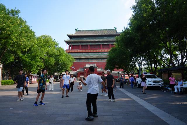 (260727) -- BEIJING, July 27, 2026 (Xinhua) -- People kick a shuttlecock at a square connecting the Drum and Bell Towers in Beijing, capital of China, July 27, 2026. Marking the second anniversary of the successful inscription of the Beijing Central Axis on the UNESCO World Heritage List, heritage sites along the central axis, such as the Palace Museum, Zhengyangmen Gate, and Altar of the God of Agriculture, also referred to as the Xiannongtan Temple, were opened to the public, and some sites launched new exhibitions on Monday.
   Stretching 7.8 kilometers from Yongding Gate in the south to the Drum and Bell Towers in the north, the Beijing Central Axis was constructed based on ancient architectural philosophies to create an ideal layout for a capital city. The Central Axis can be traced back to the early Yuan Dynasty (1271-1368), and its length was extended in the Ming and Qing dynasties. (Xinhua/Xie Han)