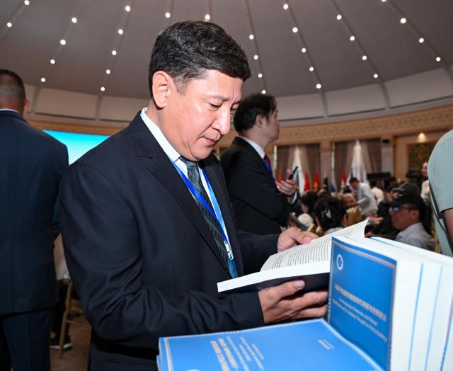 (260727) -- BISHKEK, July 27, 2026 (Xinhua) -- A participant reads a single-volume copy of the Kyrgyz and Russian versions of a think tank report titled "Contemporary Features and Global Significance of Xi Jinping Thought on Party Building" at the 2026 Shanghai Cooperation Organization (SCO) Media and Think Tank Summit in Bishkek, Kyrgyzstan, July 27, 2026.
  The 2026 Shanghai Cooperation Organization (SCO) Media and Think Tank Summit opened here on Monday, during which the Kyrgyz and Russian versions of the report were jointly issued by the National High-Level Think Tank of the Party School of the Communist Party of China (CPC) Central Committee (National Academy of Governance) and the National High-Level Think Tank of Xinhua News Agency.
  The report provides an in-depth explanation of the distinctive qualities and key factors behind the CPC's continued success and enduring vitality. (Xinhua/Feng Kaihua)