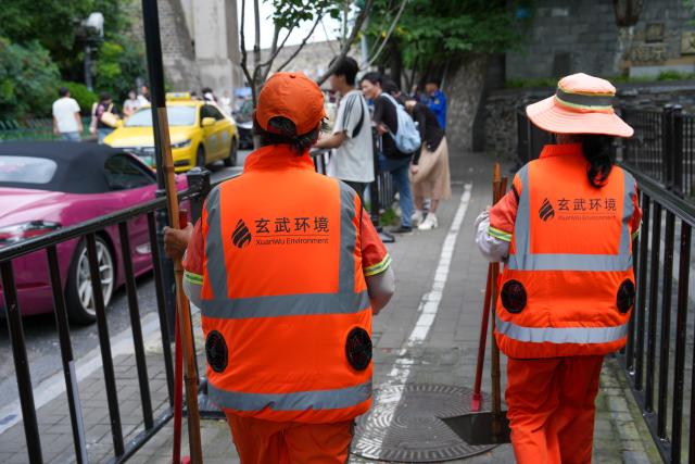 (260728) -- NANJING, July 28, 2026 (Xinhua) -- Sanitation workers in cooling vests walk on the street in Nanjing, east China's Jiangsu Province, July 28, 2026. Recently, in response to the high summer temperatures, sanitation workers in Xuanwu District of Nanjing City have been equipped with cooling vests. The vests are fitted with miniature fans on both sides of the waist, providing inward airflow. (Xinhua/Li Bo)