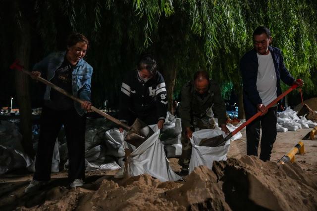 (260730) -- DUNHUANG, July 30, 2026 (Xinhua) -- Local officials and residents stack sandbags to fortify the embankment along the Danghe River in Dunhuang, northwest China's Gansu Province, July 29, 2026. The water level of the Danghe River, which runs through Dunhuang City in northwest China's Gansu Province, rose rapidly following days of heavy rainfall and increased inflows from upstream. Local personnel in Dunhuang quickly mobilized for flood control and relief operations. (Xinhua/Lang Bingbing)