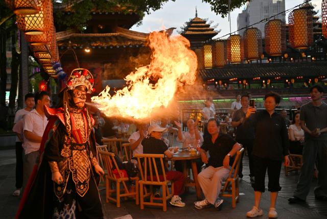 (260731) -- BEIJING, July 31, 2026 (Xinhua) -- Tourists watch a folk performance near a lounge bridge in Xuan'en County, Enshi Tujia and Miao Autonomous Prefecture, central China's Hubei Province, July 29, 2026. A series of night tours have been launched along the waterfront walkways in Xuan'en County to enrich local night tourism scenarios and invigorate the cultural and tourism vitality of the small mountain town. (Photo by Song Wen/Xinhua)