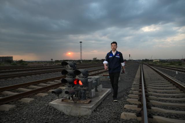 (260731) -- NAIROBI, July 31, 2026 (Xinhua) -- Communication engineer Zhou Junbing walks past a signal device of Nairobi Station on the Mombasa-Nairobi Standard Gauge Railway in Kenya on July 22, 2026. After graduating from Beijing Jiaotong University with a degree in communication engineering, Zhou Junbing joined the Africa Star Railway Operation Company (Afristar) at the age of 27, dedicating himself to the operation of Mombasa-Nairobi Standard Gauge Railway (SGR). 
  At that time, the railway had just begun operations. Thanks to Zhou's solid expertise and experience in railway communication, he quickly became a key member of a team responsible for maintaining and supporting the railway's communication system. 
  The railway stretches 472 km, linking the port city of Mombasa in the southeastern part of the country with the capital city, Nairobi. It is the first modern railway constructed in Kenya since independence and stands as a key achievement of China-Kenya cooperation under the Belt and Road Initiative. The Afristar provides operational and technical support for the Mombasa-Nairobi SGR.
  Today, Zhou is in charge of the technical support for communication equipment serving 26 railway systems along the Mombasa-Nairobi SGR. He spends much of his time on the front line of equipment maintenance and technical support. During his eight years working in Kenya, Zhou has continuously shared his expertise with local employees. Whenever the local staff encounter technical challenges, Zhou is always the first person they turn to for advice. To his Kenyan colleagues, Zhou is not only a Chinese engineer, but also a trusted mentor and friend. (Xinhua/Yang Guang)