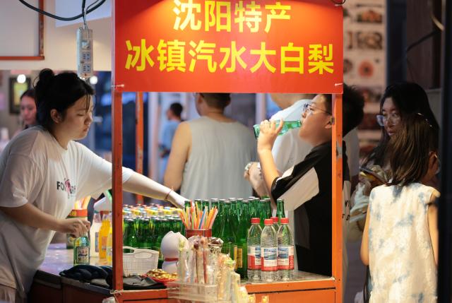 (260731) -- SHENYANG, July 31, 2026 (Xinhua) -- A tourist tastes local beverage at the Xita neighborhood in Shenyang, northeast China's Liaoning Province, July 29, 2026. Xita is a distinctive neighborhood in Shenyang which is known for its wide variety of local specialties and attracts visitors from across the country. (Xinhua/Li Gang)