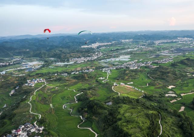 (260731) -- HUANGPING, July 31, 2026 (Xinhua) -- An aerial photo taken on July 30, 2026 shows tourists experiencing paragliding with pilots at a paragliding base in Jiuzhou Town, Huangping County, southwest China's Guizhou Province. During the summer vacation, visitors head to the paragliding base here, where they soar over the mountains with professional pilots and enjoy the cool mountain air. (Xinhua/Yang Wenbin)
