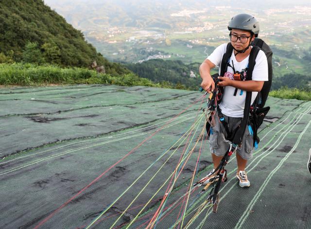 (260731) -- HUANGPING, July 31, 2026 (Xinhua) -- A pilot arranges a parachute before taking off at a paragliding base in Jiuzhou Town, Huangping County, southwest China's Guizhou Province, July 30, 2026. During the summer vacation, visitors head to the paragliding base here, where they soar over the mountains with professional pilots and enjoy the cool mountain air. (Xinhua/Yang Wenbin)