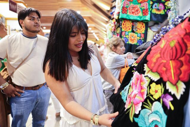 (260731) -- OAXACA, July 31, 2026 (Xinhua) -- A customer selects a hand-embroidered garment at the 2026 Guelaguetza Handicrafts Fair in Oaxaca City, Oaxaca State, Mexico, July 26, 2026. The southern Mexican state of Oaxaca is known for its handwoven textiles and embroidered garments. Local artisans make clothing, rugs and other items using weaving, dyeing and embroidery techniques. Sold at markets and handicraft fairs, these colorful creations remain part of everyday life in Oaxaca. (Xinhua/Liu Wenhui)