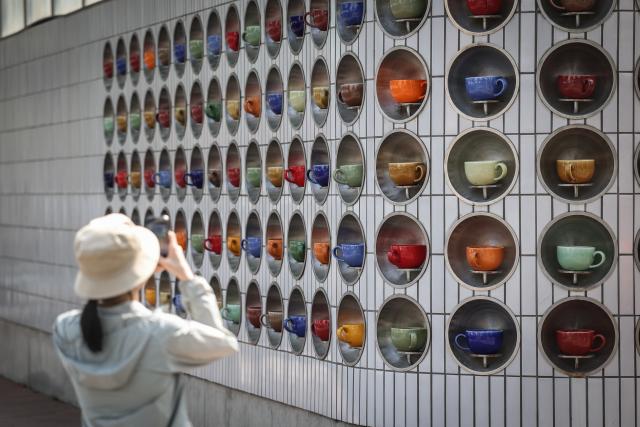 (260802) -- SHENYANG, Aug. 2, 2026 (Xinhua) -- A tourist takes a photo of an installation of coffee mugs on Bajing Street, Shenyang City, northeast China's Liaoning Province, Aug. 1, 2026. A pack of coffee shops of varying styles on Bajing Street in Shenyang have breathed new life into the old city. Once quiet but obsolete, this historic street is now a vibrant new landmark of culture and tourism that attracts thousands of young visitors every day. Each coffee shop here tells a different story of how a city grows in time. (Xinhua/Pan Yulong)