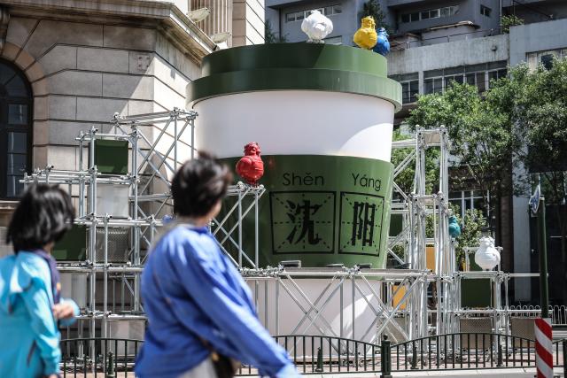 (260802) -- SHENYANG, Aug. 2, 2026 (Xinhua) -- People walk past an outdoor art installation on Bajing Street, Shenyang City, northeast China's Liaoning Province, Aug. 1, 2026. A pack of coffee shops of varying styles on Bajing Street in Shenyang have breathed new life into the old city. Once quiet but obsolete, this historic street is now a vibrant new landmark of culture and tourism that attracts thousands of young visitors every day. Each coffee shop here tells a different story of how a city grows in time. (Xinhua/Pan Yulong)