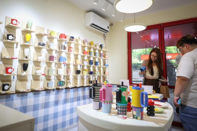 (260802) -- SHENYANG, Aug. 2, 2026 (Xinhua) -- Tourists select coffee mugs at a store on Bajing Street, Shenyang City, northeast China's Liaoning Province, Aug. 1, 2026. A pack of coffee shops of varying styles on Bajing Street in Shenyang have breathed new life into the old city. Once quiet but obsolete, this historic street is now a vibrant new landmark of culture and tourism that attracts thousands of young visitors every day. Each coffee shop here tells a different story of how a city grows in time. (Xinhua/Pan Yulong)
