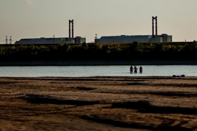 (260803) -- BUDAPEST, Aug. 3, 2026 (Xinhua) -- People cool off in the Danube River, with the Paks nuclear power plant in the background, near Dunaszentbenedek, Hungary, Aug. 2, 2026. Hungary is entering its "most critical 5 days" as dropping water levels on the Danube River threaten the complete shutdown of the Paks nuclear power plant amid an extreme heatwave, Hungary's Prime Minister Peter Magyar said on Sunday, warning that the plant could be shut down for more than a month. (Photo by David Balogh/Xinhua)