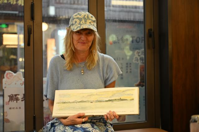 (260803) -- HANGZHOU, Aug. 3, 2026 (Xinhua) -- German art teacher Anke Deber shows a scenic picture she painted during her journey in China, in Hangzhou, east China's Zhejiang Province, July 21, 2026. (Xinhua/Liu Mingxiang)