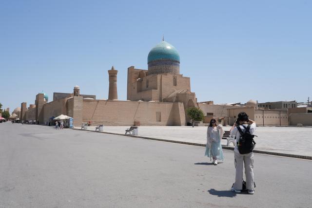 (260803) -- BUKHARA, Aug. 3, 2026 (Xinhua) -- A tourist takes photos in front of historic architecture in Bukhara, Uzbekistan, Aug. 3, 2026. The historic city of Bukhara in southwestern Uzbekistan is currently gripping with severe heat, with daytime highs consecutively exceeding 35 degrees Celsius. (Photo by Zafar Khalilov/Xinhua)