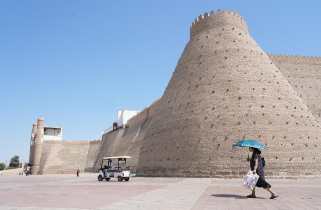 (260803) -- BUKHARA, Aug. 3, 2026 (Xinhua) -- A pedestrian carries an umbrella to shield herself from the sun in front of the Ark of Bukhara in Bukhara, Uzbekistan, Aug. 3, 2026. The historic city of Bukhara in southwestern Uzbekistan is currently gripping with severe heat, with daytime highs consecutively exceeding 35 degrees Celsius. (Photo by Zafar Khalilov/Xinhua)