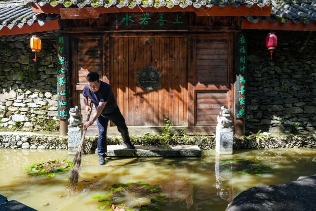 (260804) -- KANGXIAN, Aug. 4, 2026 (Xinhua) -- A homestay owner clears fallen leaves at a fish pond in Kangxian County of Longnan City, northwest China's Gansu Province, Aug. 4, 2026. Kangxian, which suffered from heavy rainfall recently, has initiated campaigns to clear up rivers and restore drinking water facilities in the county, striving to bring people's work and daily life back to normal. (Xinhua/Lang Bingbing)