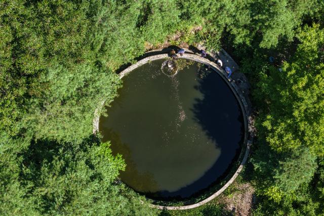 (260804) -- KANGXIAN, Aug. 4, 2026 (Xinhua) -- An aerial drone photo shows villagers clearing floating debris from an irrigation pond at Zhangjiahe Village of Kangxian County in Longnan City, northwest China's Gansu Province, Aug. 4, 2026. Kangxian, which suffered from heavy rainfall recently, has initiated campaigns to clear up rivers and restore drinking water facilities in the county, striving to bring people's work and daily life back to normal. (Xinhua/Lang Bingbing)