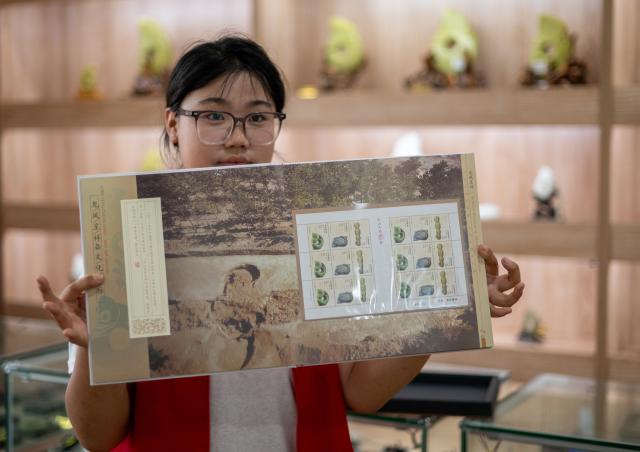 (260804) -- CHAOYANG, Aug. 4, 2026 (Xinhua) -- A staff member shows Hongshan culture-themed stamps at the Niuheliang site museum within the Niuheliang national archaeological relic site park in Chaoyang City, northeast China's Liaoning Province, Aug. 4, 2026. The Niuheliang national archaeological relic site park was built on the Niuheliang site, a large-scale prehistoric ritual and burial complex featuring the temple of the goddess, altars and stone tombs. Dating back more than 5,000 years, the site unearthed stone tools, pottery and jade artifacts with dragon, phoenix and human motifs, reflecting the rituals and beliefs of the Hongshan culture. (Xinhua/Hu Jingwen)
