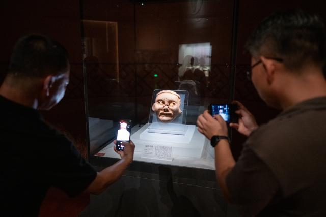 (260804) -- CHAOYANG, Aug. 4, 2026 (Xinhua) -- People take photos of a replica of the clay facial sculpture of goddess at the Niuheliang site museum within the Niuheliang national archaeological relic site park in Chaoyang City, northeast China's Liaoning Province, Aug. 4, 2026. The Niuheliang national archaeological relic site park was built on the Niuheliang site, a large-scale prehistoric ritual and burial complex featuring the temple of the goddess, altars and stone tombs. Dating back more than 5,000 years, the site unearthed stone tools, pottery and jade artifacts with dragon, phoenix and human motifs, reflecting the rituals and beliefs of the Hongshan culture. (Xinhua/Hu Jingwen)