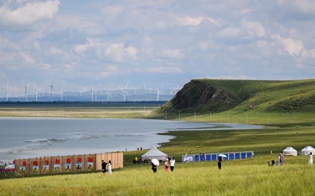 (260804) -- XILIN GOL, Aug. 4, 2026 (Xinhua) -- Tourists play by Baiyin Chagan Lake, or "Milky Lake," in Xilin Gol League, north China's Inner Mongolia Autonomous Region, Aug. 4, 2026. The lake is dubbed "Milky Lake" as tiny mineral particles float in the water, turning it creamy-white like milk. (Xinhua/Lian Zhen)