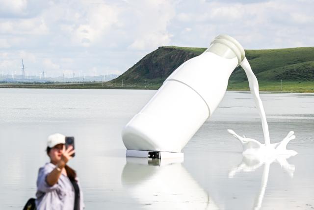 (260804) -- XILIN GOL, Aug. 4, 2026 (Xinhua) -- A tourist takes a selfie by Baiyin Chagan Lake, or "Milky Lake," in Xilin Gol League, north China's Inner Mongolia Autonomous Region, Aug. 4, 2026. The lake is dubbed "Milky Lake" as tiny mineral particles float in the water, turning it creamy-white like milk. (Xinhua/Lian Zhen)
