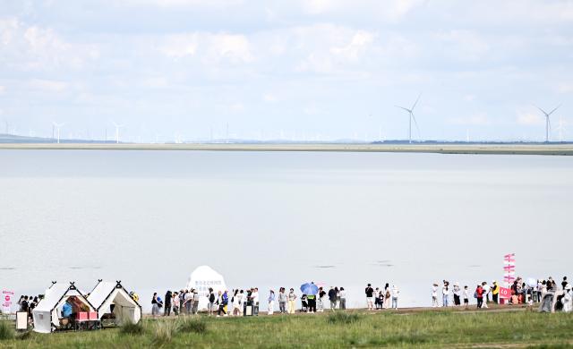 (260804) -- XILIN GOL, Aug. 4, 2026 (Xinhua) -- Tourists visit Baiyin Chagan Lake, or "Milky Lake," in Xilin Gol League, north China's Inner Mongolia Autonomous Region, Aug. 4, 2026. The lake is dubbed "Milky Lake" as tiny mineral particles float in the water, turning it creamy-white like milk. (Xinhua/Lian Zhen)