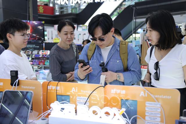 (260805) -- SHENZHEN, Aug. 5, 2026 (Xinhua) -- This photo taken on June 24, 2026 shows tourists from South Korea experiencing AI translator at Huaqiangbei of Shenzhen, south China's Guangdong Province. With the deep application of the achievements of emerging industries, many inbound foreign tourists choose science and technology tour as the theme of their journey in the Chinese cities. 
  In Shenzhen, foreign tourists are attracted by AI applications and technology scenarios in daily life, such as AI glasses, smart robots and unmanned delivery service. (Xinhua/Liang Xu)