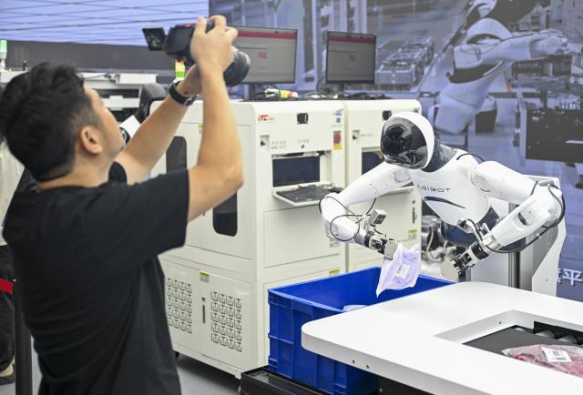 (260805) -- SHANGHAI, Aug. 5, 2026 (Xinhua) -- A visitor takes photos of a humanoid robot at AGIBOT, an embodied AI company, in Shanghai, east China, Aug. 4, 2026. In Shanghai's tech companies like AGIBOT and Maniformer, embodied intelligence robots are trained in household, retail, sorting, production and other real-world scenarios, to advance their AI capabilities for real-life use. (Xinhua/Liu Ying)