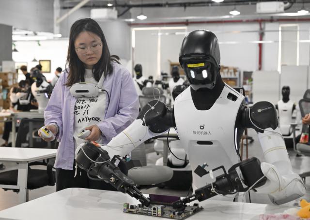 (260805) -- SHANGHAI, Aug. 5, 2026 (Xinhua) -- A staff member trains a robot to work at a production line at Maniformer, a physical AI data service platform, in Shanghai, east China, Aug. 5, 2026. In Shanghai's tech companies like AGIBOT and Maniformer, embodied intelligence robots are trained in household, retail, sorting, production and other real-world scenarios, to advance their AI capabilities for real-life use. (Xinhua/Liu Ying)