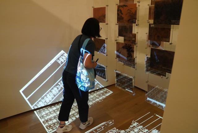 (260806) -- NEW YORK, Aug. 6, 2026 (Xinhua) -- A visitor views ancient paintings with lyric poetry from the Song Dynasty (960-1127) projected on the floor during "The Unheard Melody: Exhibition of Music in Chinese Paintings" in New York, the United States, Aug. 5, 2026. The exhibition opened here on Wednesday. Featuring musical imagery from the art of ancient Chinese painting, it showcases a curated selection of masterpieces inspired by music from the Song Dynasty (960-1127), and invites visitors to explore the sounds and stories embedded within the artworks. (Xinhua/Zhang Fengguo)