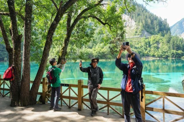(260806) -- JIUZHAIGOU, Aug. 6, 2026 (Xinhua) -- Tourists from South Korea take photos at the Jiuzhaigou scenic spot in southwest China's Sichuan Province, Aug. 6, 2026. Jiuzhaigou is known for its spectacular waterfalls, lush forests, serene plateau lakes and karst rock formations, making it a popular destination for international tourists. (Xinhua/Wang Xi)