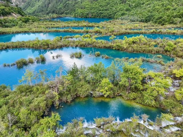 (260806) -- JIUZHAIGOU, Aug. 6, 2026 (Xinhua) -- A drone photo taken on Aug. 5, 2026 shows a view at the Jiuzhaigou scenic spot in southwest China's Sichuan Province. Jiuzhaigou is known for its spectacular waterfalls, lush forests, serene plateau lakes and karst rock formations, making it a popular destination for international tourists. (Xinhua/Wang Xi)