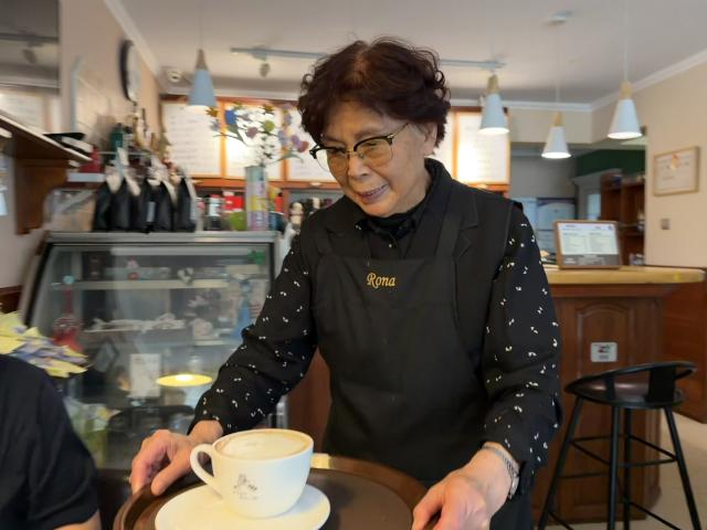 (260807) -- QINGDAO, Aug. 7, 2026 (Xinhua) -- Zhao Qiying serves coffee at Rona Coffee in Qingdao, east China's Shandong Province, June 15, 2026. TO GO WITH "Feature: Cafe's success serves to bring wider world to 86-year-old proprietor" (Xinhua/Zhang Liyuan)