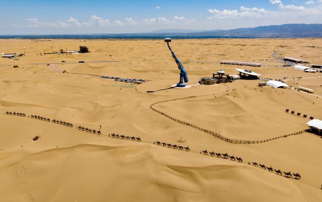 (260807) -- ZHONGWEI, Aug. 7, 2026 (Xinhua) -- An aerial drone photo taken on Aug. 6, 2026 shows tourists visiting the Shapotou scenic area in Zhongwei, northwest China's Ningxia Hui Autonomous Region. The Shapotou scenic area features a unique landscape where desert, the Yellow River, mountain and oasis converge. During the peak summer tourism season, the scenic area has witnessed a surge in visitors, with daily arrivals exceeding 20,000 at its peak. (Xinhua/Yang Zhisen)