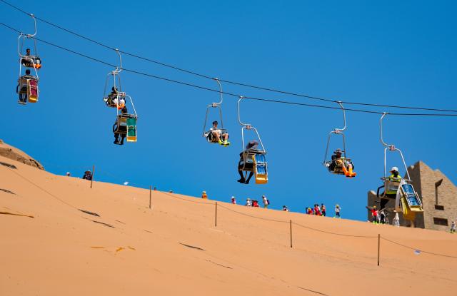 (260807) -- ZHONGWEI, Aug. 7, 2026 (Xinhua) -- Tourists ride cable cars at the Shapotou scenic area in Zhongwei, northwest China's Ningxia Hui Autonomous Region, Aug. 6, 2026. The Shapotou scenic area features a unique landscape where desert, the Yellow River, mountain and oasis converge. During the peak summer tourism season, the scenic area has witnessed a surge in visitors, with daily arrivals exceeding 20,000 at its peak. (Xinhua/Yang Zhisen)