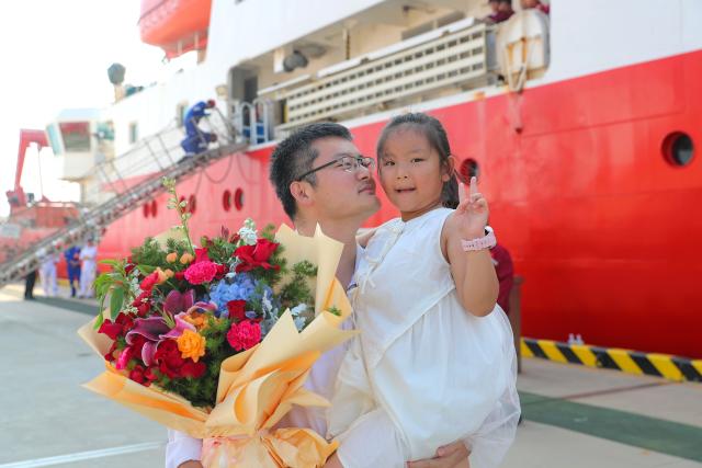 (260807) -- QINGDAO, Aug. 7, 2026 (Xinhua) -- Liang Xixiang, a member of the scientific expedition aboard China's comprehensive research vessel KEXUE, holds his daughter at a wharf base in Qingdao, east China's Shandong Province, Aug. 7, 2026. KEXUE docked at a wharf base of the Institute of Oceanology under the Chinese Academy of Sciences on Friday, marking the conclusion of a shared research cruise in the western Pacific after a 35-day voyage covering 5,845 nautical miles. The data and samples obtained during the cruise will provide scientific support for more accurate typhoon forecasting and global climate change research. (Photo by Zhang Jingang/Xinhua)