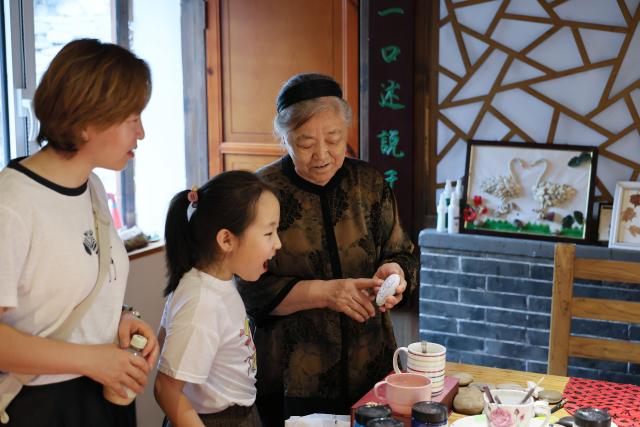 (260808) -- TIANJIN, Aug. 8, 2026 (Xinhua) -- Liu Anqin (R) introduces her artwork at her homestay in Xijingyu Village of Jizhou District, north China's Tianjin, Aug. 4, 2026. Liu Anqin, 82, never expected that retirement would open a new chapter in her life.
   Born in northeast China's Heilongjiang Province, Liu had no formal training in painting. After retirement, she enrolled in painting classes at an education program for the elderly and discovered her passion for art. Six years ago, Liu moved to Tianjin with her son. This spring, she rented a courtyard in Xijingyu Village and opened a homestay. Inspired by the village's rustic charm and stony landscape, Liu began painting on stones.
   Unlike painting on paper, stone painting is more challenging and requires greater patience. Yet Liu enjoys the process. Just months later, the courtyard is no longer just a homestay; it has become a small art gallery that attracts visitors to take photos and appreciate stone paintings.
   For Liu, meeting new friends and sharing her passion for art with young people is always a delight. "It's never too late to start something new, as long as you enjoy it," she said. (Xinhua/Li Ran)
