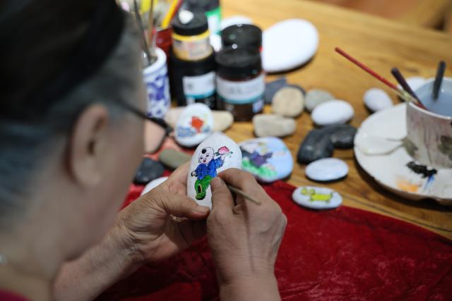 (260808) -- TIANJIN, Aug. 8, 2026 (Xinhua) -- Liu Anqin works on a stone-painting work at Xijingyu Village of Jizhou District in north China's Tianjin, Aug. 5, 2026. Liu Anqin, 82, never expected that retirement would open a new chapter in her life.
   Born in northeast China's Heilongjiang Province, Liu had no formal training in painting. After retirement, she enrolled in painting classes at an education program for the elderly and discovered her passion for art. Six years ago, Liu moved to Tianjin with her son. This spring, she rented a courtyard in Xijingyu Village and opened a homestay. Inspired by the village's rustic charm and stony landscape, Liu began painting on stones.
   Unlike painting on paper, stone painting is more challenging and requires greater patience. Yet Liu enjoys the process. Just months later, the courtyard is no longer just a homestay; it has become a small art gallery that attracts visitors to take photos and appreciate stone paintings.
   For Liu, meeting new friends and sharing her passion for art with young people is always a delight. "It's never too late to start something new, as long as you enjoy it," she said. (Xinhua/Li Ran)