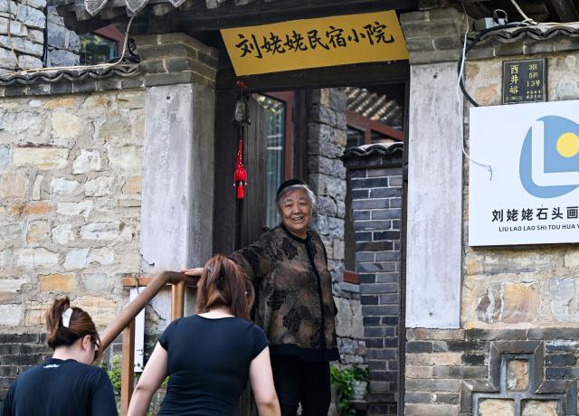 (260808) -- TIANJIN, Aug. 8, 2026 (Xinhua) -- Liu Anqin welcomes visitors at her homestay in Xijingyu Village of Jizhou District, north China's Tianjin, Aug. 4, 2026. Liu Anqin, 82, never expected that retirement would open a new chapter in her life.
   Born in northeast China's Heilongjiang Province, Liu had no formal training in painting. After retirement, she enrolled in painting classes at an education program for the elderly and discovered her passion for art. Six years ago, Liu moved to Tianjin with her son. This spring, she rented a courtyard in Xijingyu Village and opened a homestay. Inspired by the village's rustic charm and stony landscape, Liu began painting on stones.
   Unlike painting on paper, stone painting is more challenging and requires greater patience. Yet Liu enjoys the process. Just months later, the courtyard is no longer just a homestay; it has become a small art gallery that attracts visitors to take photos and appreciate stone paintings.
   For Liu, meeting new friends and sharing her passion for art with young people is always a delight. "It's never too late to start something new, as long as you enjoy it," she said. (Xinhua/Zhao Zishuo)