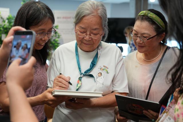 (260809) -- OTTAWA, Aug. 9, 2026 (Xinhua) -- Chinese illustrator Cai Gao (C) signs books for readers at a meet-and-greet event in Ottawa, Canada, Aug. 8, 2026. On Aug. 7, Cai received the 2026 Hans Christian Andersen Award for Illustration at a ceremony in Ottawa, becoming the first Chinese illustrator to win the highest international honor for creators of children's books. (Photo by Chen Min/Xinhua)