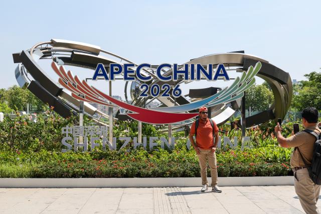 (260810) -- SHENZHEN, Aug. 10, 2026 (Xinhua) -- A foreign tourist poses for photos with a themed installation at the east square of the Shenzhen North Railway Station in Shenzhen, south China's Guangdong Province, Aug. 10, 2026. With themed bulletin boards, outdoor posts, decorations and installations, Shenzhen marked on Monday the 100-day countdown to the 33rd Asia-Pacific Economic Cooperation (APEC) Economic Leaders' Meeting. (Xinhua/Liang Xu)