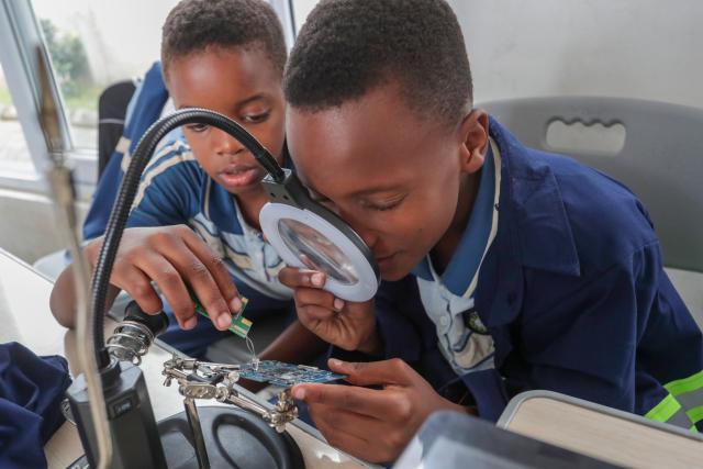 (260811) -- DAR ES SALAAM, Aug. 11, 2026 (Xinhua) -- Students inspect circuit boards using a magnifying glass during a practical skills class at De'kayra Pre and Primary School in Bagamoyo, Tanzania, Aug. 7, 2026. TO GO WITH "Feature: Learning by doing prepares Tanzanian children for future" (Xinhua/Emmanuel Herman)