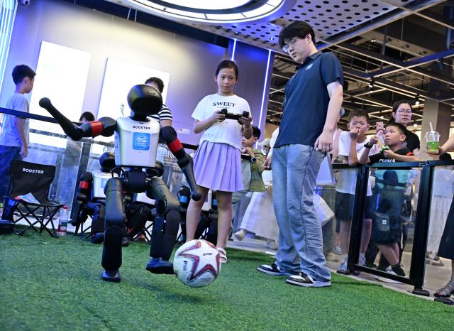 (260811) -- QINGDAO, Aug. 11, 2026 (Xinhua) -- A girl controls a robot to play football at a robot 6S experience store in Qingdao, east China's Shandong Province on Aug. 11, 2026. Recently, the first robot 6S experience store in Qingdao opened, attracting a large number of consumers to visit and experience. This store integrates six major functions including sale, spare parts, service, survey, lease and personalized customization, helping further introducing robots into people's lives. (Xinhua/Li Ziheng)