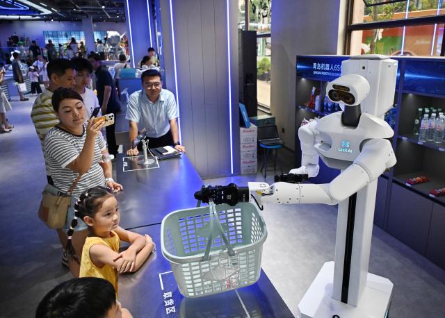(260811) -- QINGDAO, Aug. 11, 2026 (Xinhua) -- People interact with a robot at a robot 6S experience store in Qingdao, east China's Shandong Province on Aug. 11, 2026. Recently, the first robot 6S experience store in Qingdao opened, attracting a large number of consumers to visit and experience. This store integrates six major functions including sale, spare parts, service, survey, lease and personalized customization, helping further introducing robots into people's lives. (Xinhua/Li Ziheng)