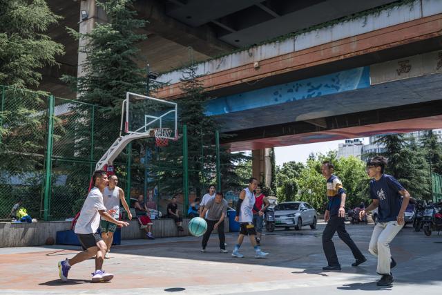 (260811) -- KUNMING, Aug. 11, 2026 (Xinhua) -- People play basketball beneath a flyover in Kunming, southwest China's Yunnan Province, Aug. 11, 2026. In recent years, Kunming has transformed some vacant areas beneath urban bridges and flyovers into public spaces for greenery, leisure, recreation and physical exercises, making the city more livable for residents. (Xinhua/Wang Guansen)