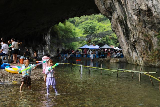 (260811) -- GUIYANG, Aug. 11, 2026 (Xinhua) -- Children have fun inside a karst cave in Kaili City, Qiandongnan Miao and Dong Autonomous Prefecture, southwest China's Guizhou Province, Aug. 8, 2026. Best known for its karst landscape, Guizhou has made the best of karst caves to develop distinctive sites for cooling retreats. Featuring natural geological wonders, cooling enjoyment and water amusements, this emerging tourist experience has become a hit among locals and visitors alike. (Photo by Wu Xianyan/Xinhua)