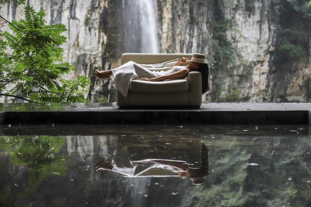 (260811) -- GUIYANG, Aug. 11, 2026 (Xinhua) -- A tourist enjoys herself at a cafe near a waterfall in Anshun City, southwest China's Guizhou Province, Aug. 6, 2026. Best known for its karst landscape, Guizhou has made the best of karst caves to develop distinctive sites for cooling retreats. Featuring natural geological wonders, cooling enjoyment and water amusements, this emerging tourist experience has become a hit among locals and visitors alike. (Photo by Lu Wei/Xinhua)